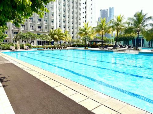a large swimming pool with palm trees and buildings at Modern Stays Makati Pool View Jazz Residences in Manila