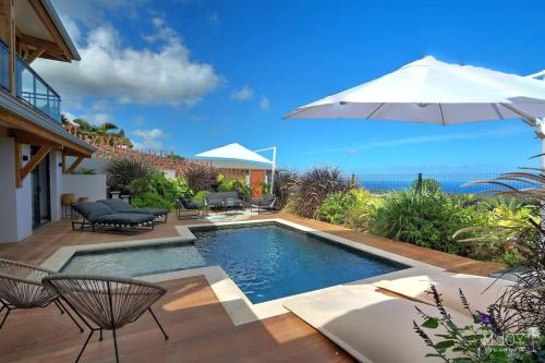 a swimming pool with chairs and an umbrella at Villa Austral et Lagons in Étang-Salé