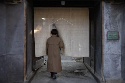 a man in a long coat looking at a drawing on a wall at Shirafuji in Suzaka