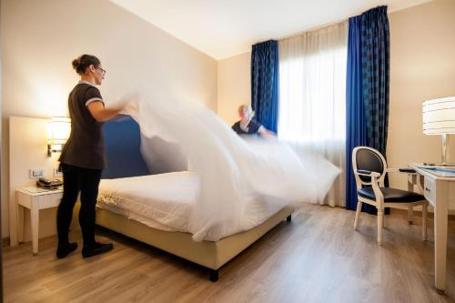 two women making a bed in a hotel room at Just Hotel Lomazzo Fiera in Lomazzo