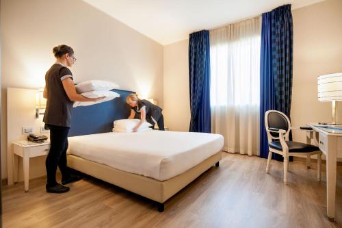 a woman is making a bed in a hotel room at Just Hotel Lomazzo Fiera in Lomazzo