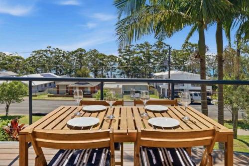 a wooden table with wine glasses on a deck at Portside at The Arc by Experience Jervis Bay in Vincentia