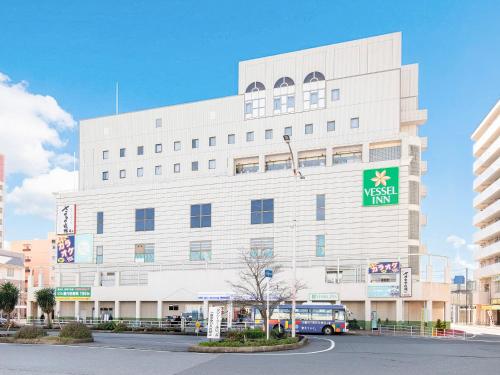 a white building with a bus parked in front of it at Vessel Inn Yachiyo Katsudai Station in Yachiyo