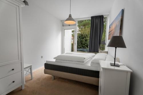 a white bedroom with a bed and a window at Erdgeschoss-Wohnung nahe am Meer in Cadzand