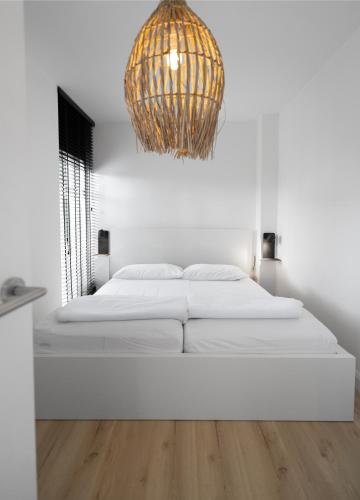 a white bedroom with a bed and a chandelier at Heggerank 5a in Nieuwvliet