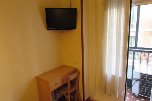 Habitación con escritorio y TV en la pared. en Hostal Prim, en Madrid