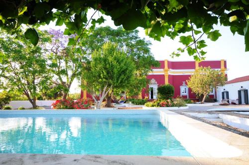 a swimming pool in front of a red building at Hortas de Baixo, Luz de Tavira in Tavira