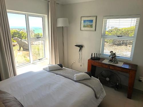 a bedroom with a bed and a desk and windows at Agulhas Splendour in Agulhas