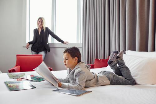 a little boy laying on a bed with a laptop at Novotel Basel City in Basel