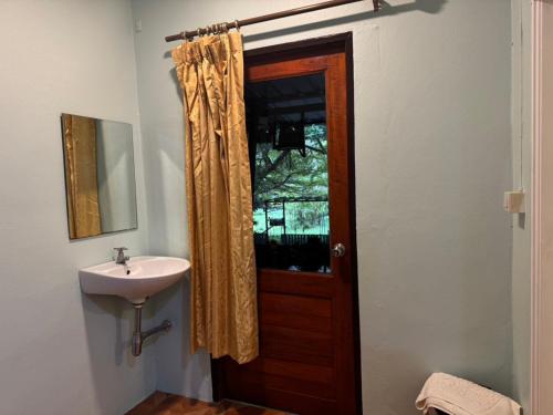 a bathroom with a sink and a wooden door at Baan Kao Kod in Nakhon Si Thammarat