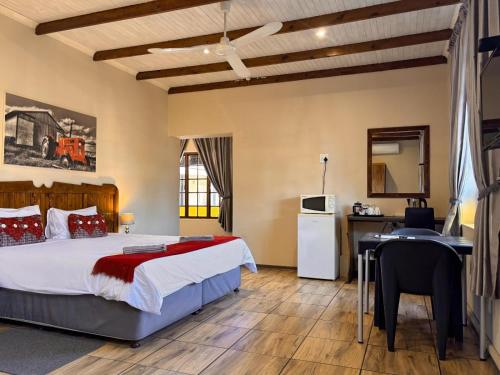 a bedroom with a bed and a desk and a kitchen at Hendersons Lodge Ltd in Senekal