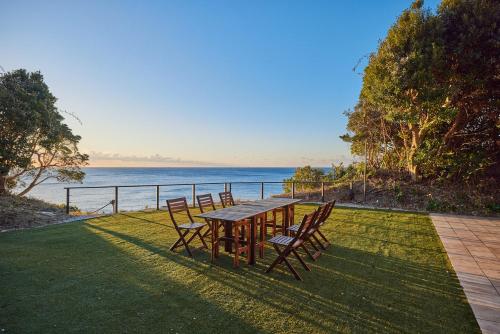 a wooden table and chairs on a lawn with the ocean at UMIBE IseShima in Shima