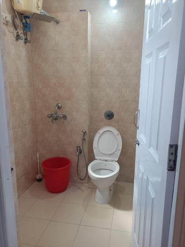 a bathroom with a toilet and a red bucket at 1 bhk apartment ruby residency in Canacona
