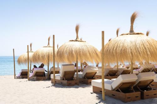 a group of chairs and straw umbrellas on a beach at Higuerón Hotel Málaga, Curio Collection by Hilton in Fuengirola