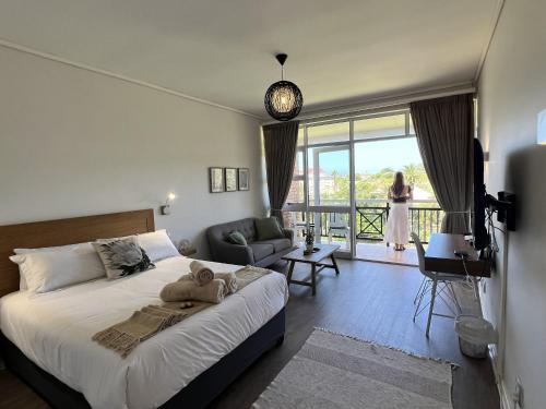 a bedroom with a bed and a woman standing on a balcony at Ocean Daze Brookes Hill Suites - Beachfront Flat in Summerstrand