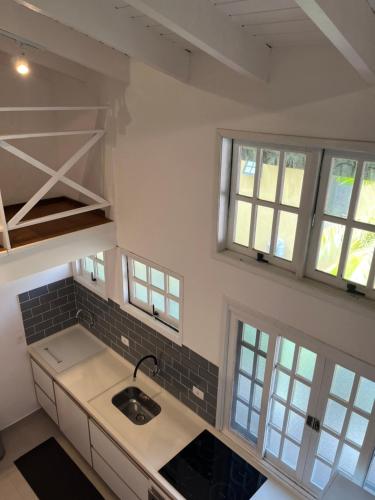 a kitchen with white counters and windows and a sink at Flat Duplex Premium - Maresias - 150m da Praia Piscina, Wi-Fi e Garagem in São Sebastião