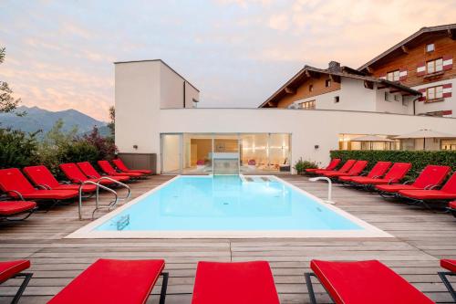 ein Pool mit roten Stühlen und ein Gebäude in der Unterkunft Familotel Amiamo in Zell am See