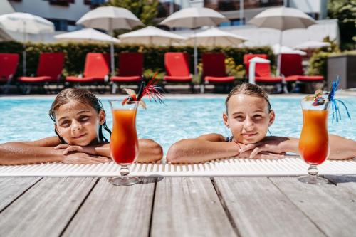 Zwei Kinder liegen mit Getränken in einem Schwimmbecken. in der Unterkunft Familotel Amiamo in Zell am See