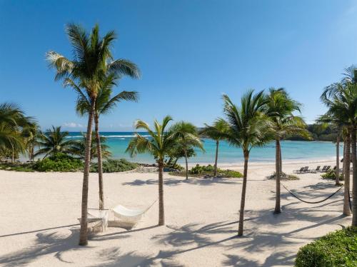 a beach with palm trees and a white chair at Conrad Tulum Riviera Maya in Tulum
