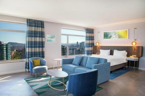 a hotel room with a bed and a couch and chairs at Hilton Diagonal Mar Barcelona in Barcelona