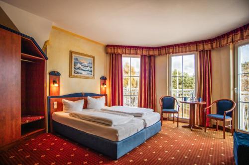 a bedroom with a bed and a table and windows at Hotel Ostseeblick - direkt hinter den Dünen in Karlshagen