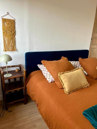 a bed with an orange blanket and a side table at Appartements Lambotte in LʼAigle
