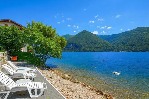 a row of white chairs sitting on the shore of a lake at Villa L'Approdo in Porlezza