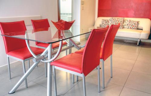 a glass table with red chairs and a couch at Dunas I, 3 in Pinamar