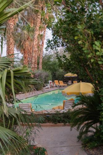a swimming pool with chairs and umbrellas at The Good House- Hot Spring Hideaway in Desert Hot Springs