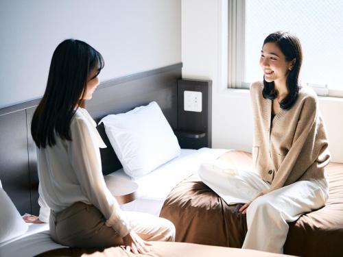 two women sitting on a bed talking to each other at Urbain Tokyo Ueno Kitasenju in Tokyo