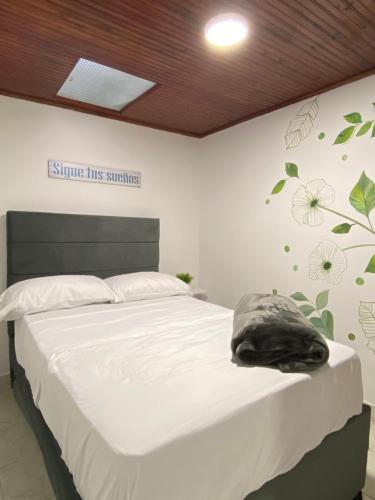 a bedroom with a bed with white sheets and flowers on the wall at Hostal Amelia Filandia in Filandia
