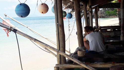a man sitting on a porch looking at the beach at Lanta New Beach Bungalows - SHA Plus in Ko Lanta