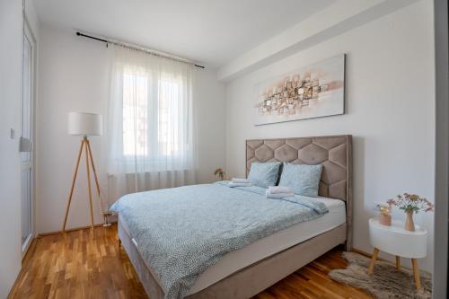a white bedroom with a large bed with blue sheets at HM Apartments in Inđija