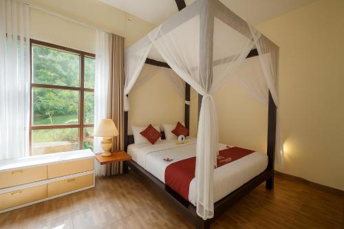 a bedroom with a canopy bed and a window at Puri Saron Hotel Madangan - Gianyar in Gianyar