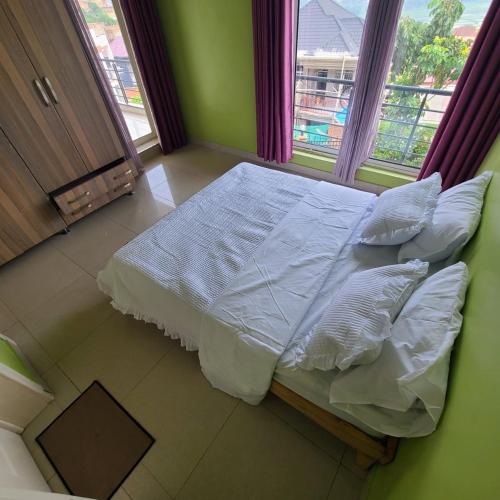 ein Bett mit weißen Laken und Kissen in einem Zimmer mit Fenster in der Unterkunft La vila viollette in Kigali