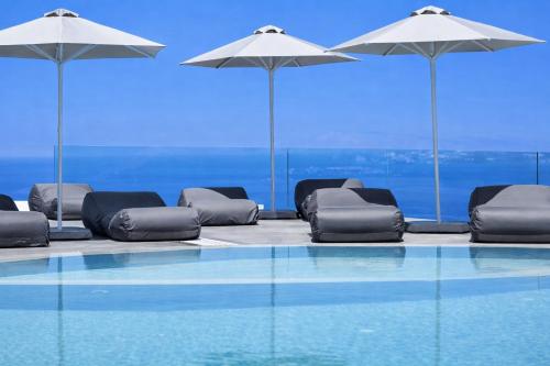 a swimming pool with chairs and umbrellas at Hotiday Santorini Oia in Oia