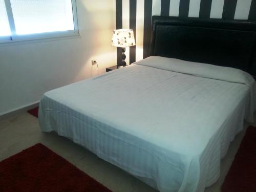 a bedroom with a white bed with a lamp and a window at Perle de Tamaris in Dar Bouazza