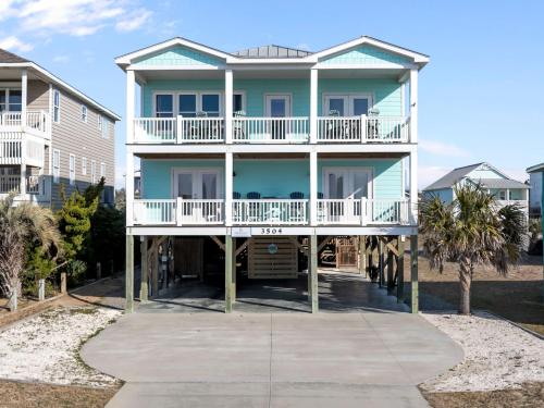 a large blue house with a balcony and palm trees at Ocean Views with Heated Pool One Row from Beach in Oak Island