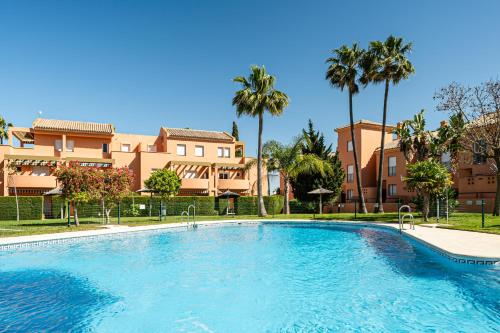 a large swimming pool with palm trees and buildings at Jardín del Golf2 9 1A in Novo Sancti Petri