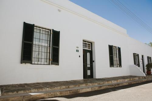 a white building with black shuttered windows at Charming Historical Cottage in Graaff-Reinet