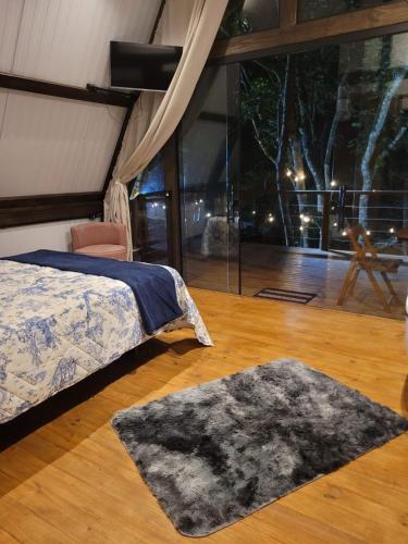 a bedroom with a bed and a rug on a wooden floor at Chalé Malbec, Estrada do Vinho com cafe da manha e hidro in São Roque