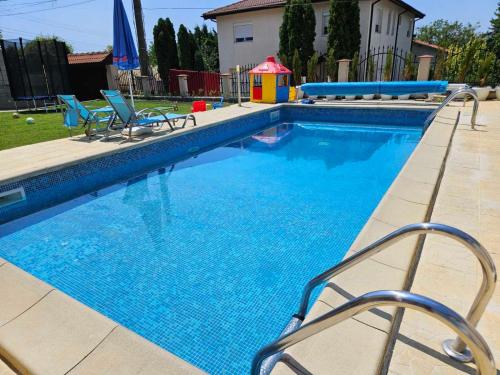 a swimming pool with two chairs and a playground at Helena Guest House - Pool & Sea View in Balchik