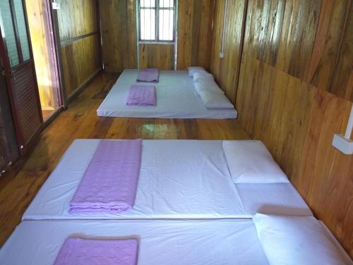 three beds in a wooden room with purple sheets at Quang Hưng Hommestay in Pac Ngoi