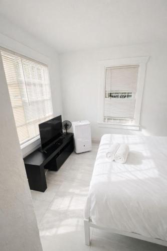 a white bedroom with a bed and a desk and two windows at Omaha Wynwood in Miami