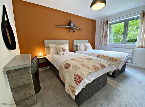 a bedroom with two beds and a clock on the wall at Byre 2 In The Park in Callander