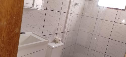 a white tiled bathroom with a toilet and a window at Casa condomínio clube in Araruama