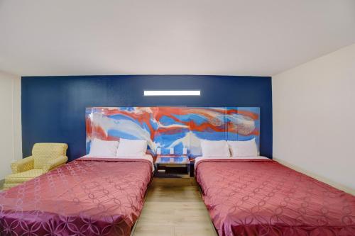 two beds in a room with a painting on the wall at Texas Inn Brownsville by Hotel O in Brownsville