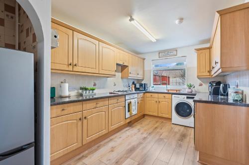 a kitchen with wooden cabinets and a washer and dryer at Spacious White House with parking, garden, Wi-Fi in Telford