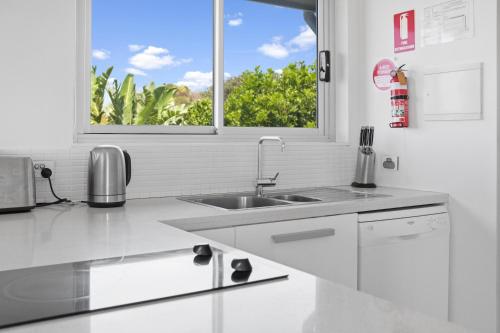eine weiße Küche mit Spüle und Fenster in der Unterkunft Beachfront Family Apt - Ocean Views in Diamond Beach