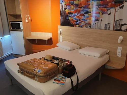 a bed with a suitcase and a hat on it at KYRIAD DIRECT LYON NORD - Dardilly in Dardilly